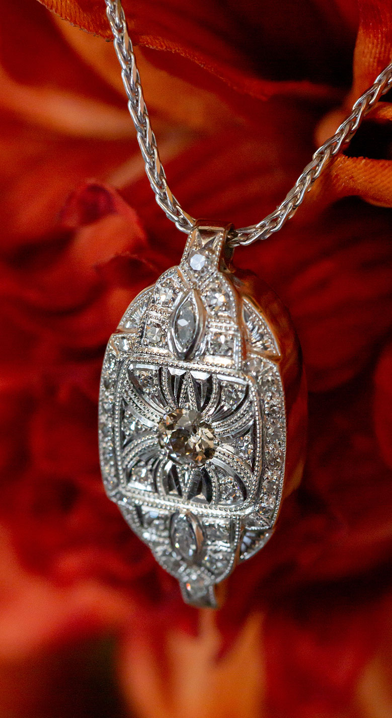 a white gold pendant with hand engraving details and diamonds mounted in it